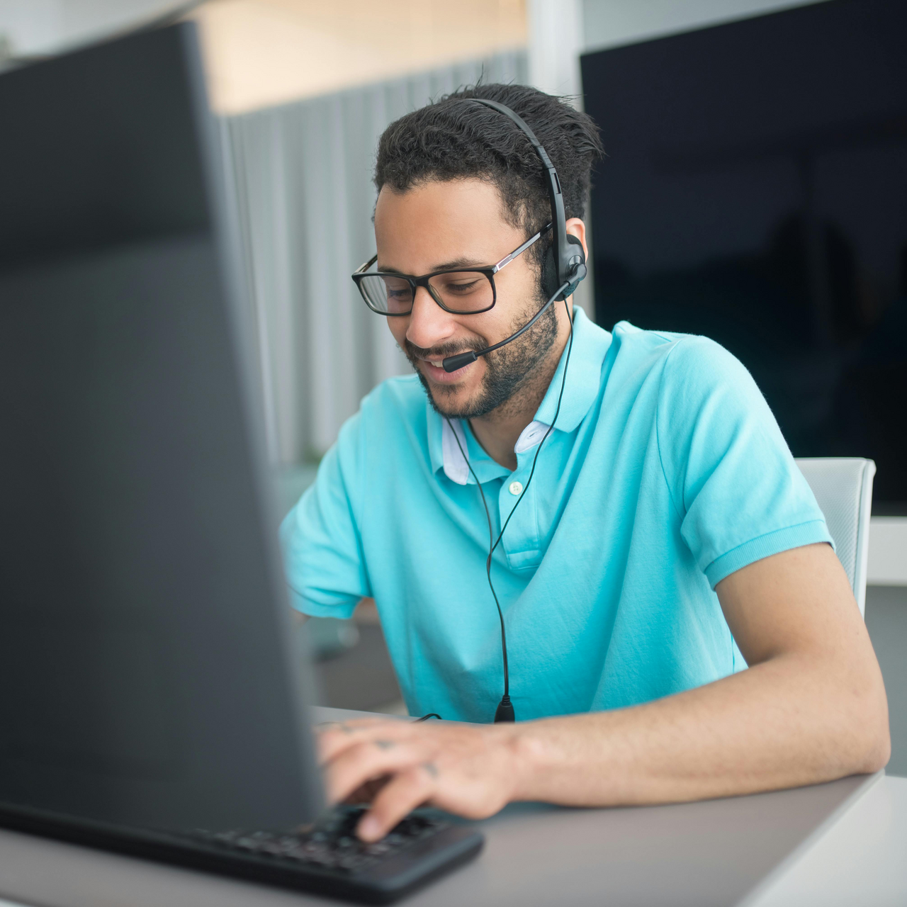 Smiling man with a headset looking down at his laptop.