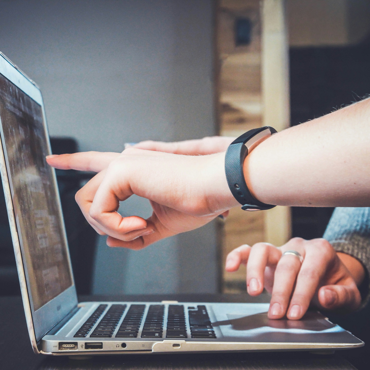 Hands pointing to a laptop screen. Another hand on the laptop mouse.