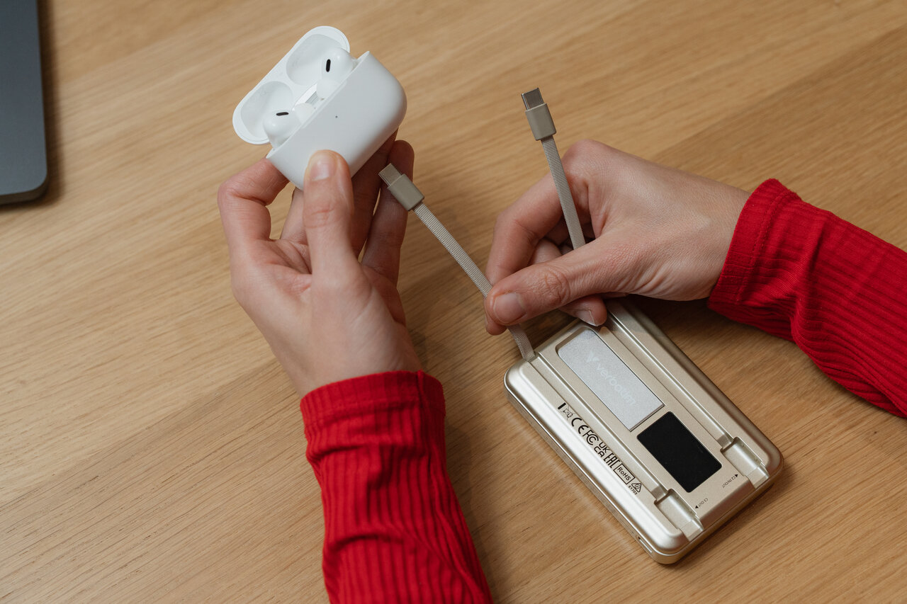 Gold power bank on a table. Hand showing the 2 integrated USB-C cables, one being plugged into an AirPods case.