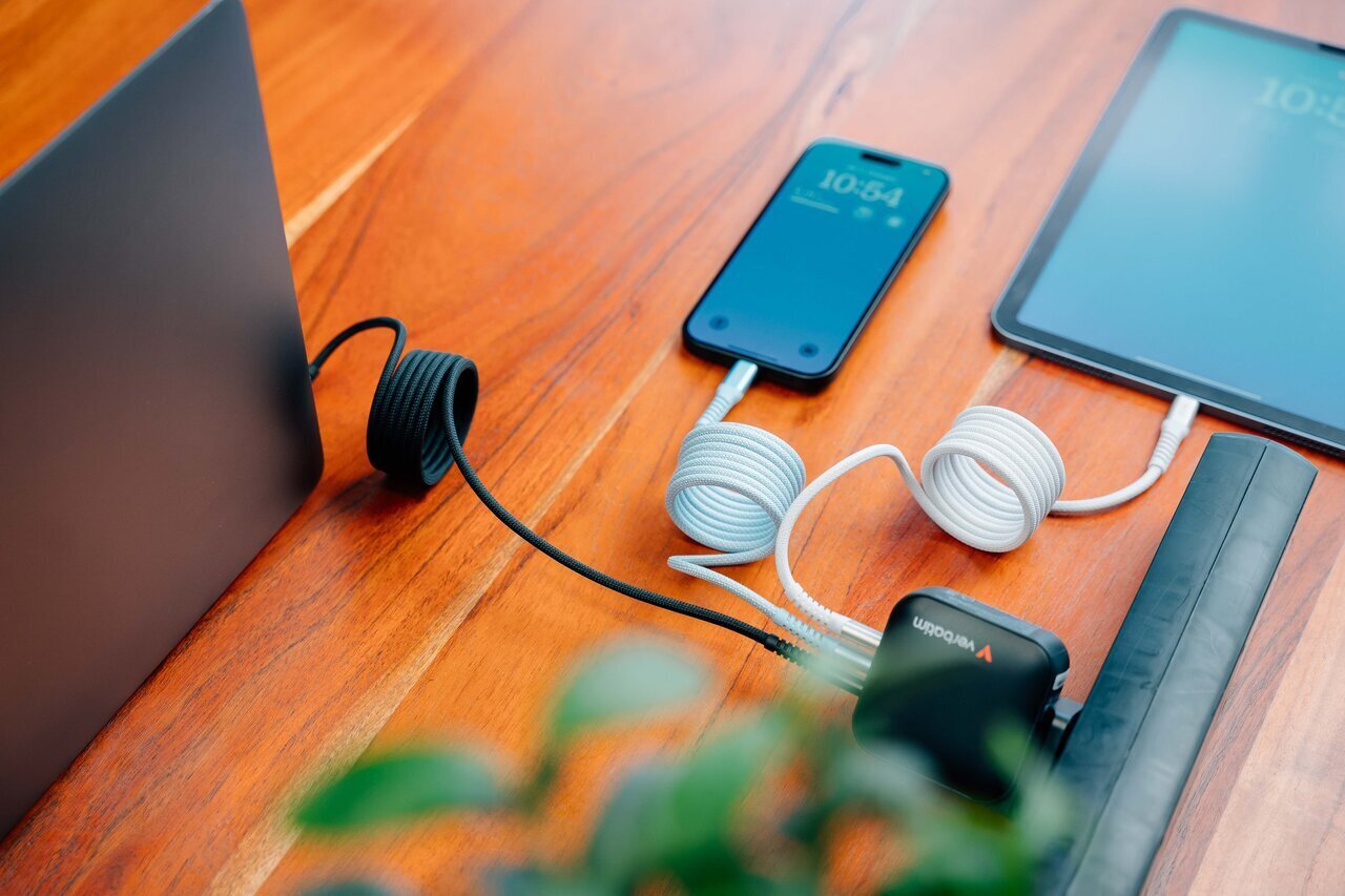 Three magnetic cables plugged into a laptop, phone and ipad on a wooden desk. All plugged into a Verbatim charging plug.