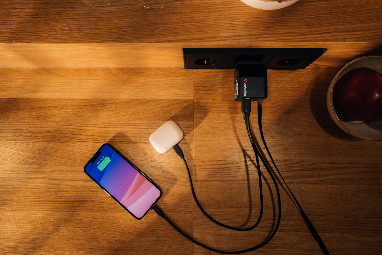 Wooden desk with a charger plugged into the wall, 3 cables plugged into it. 1 cable charging a phone, another charging ipods.