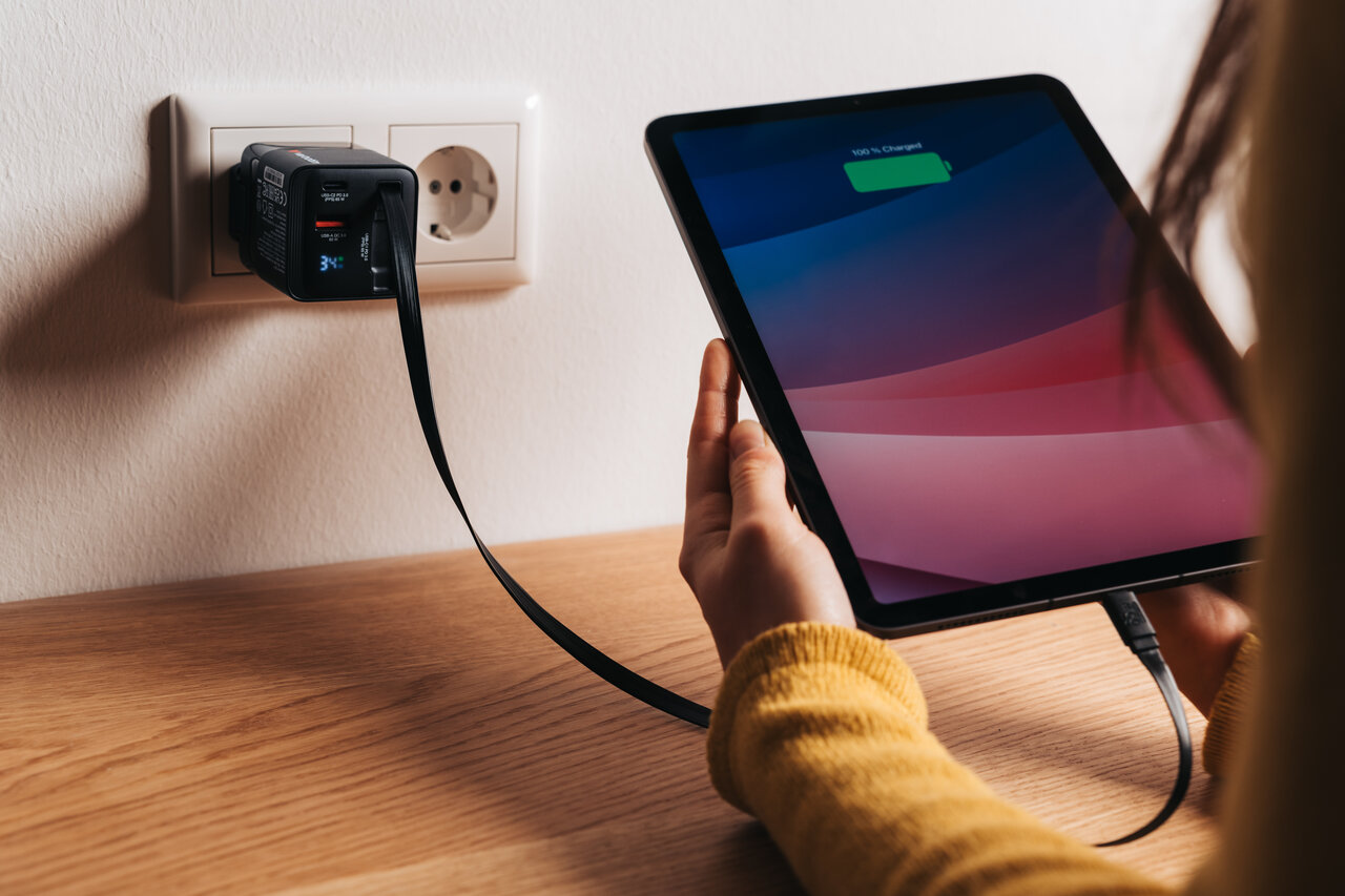 Woman holding an iPad that is charging via a cable and GaN Charger plugged into an EU wall socket